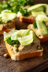  Open sandwiches with pate, cucumber, capers, and parsley on a old cutting board.