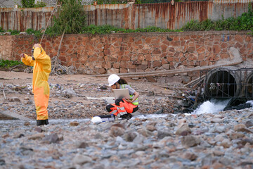 Environmental field team in protective gear analyzes water samples on a polluted beach. One holds a...
