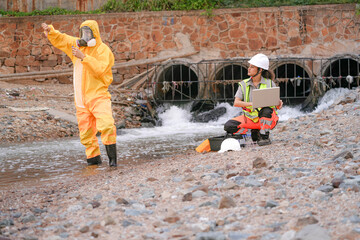 Environmental field team in protective gear analyzes water samples on a polluted beach. One holds a...