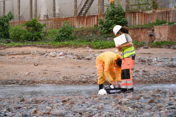 Environmental field team in protective gear analyzes water samples on a polluted beach. One holds a...