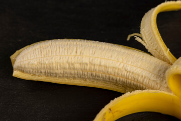one open ripe yellow banana on a black slate board, ripe and sweet yellow banana on a kitchen board...