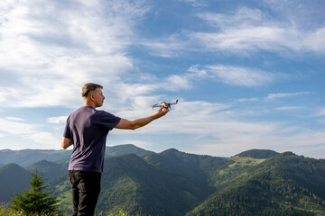 Man launching drone in mountain landscape. A man prepares to launch a drone while standing on a...