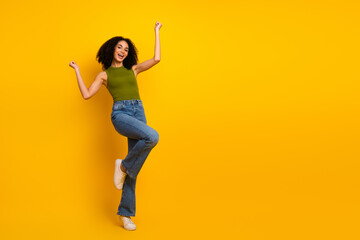 Fashionable young woman in casual attire smiling and posing energetically against a vibrant yellow background, expressing joy