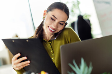 Confident businesswoman multitasking during work at modern office workspace with documents, laptop,...