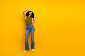 Casual young woman striking a cheerful pose in green top and jeans on yellow background, embodying...