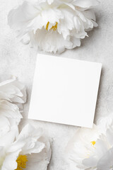 Blank wedding invitation mockup with copy space surrounded by elegant white peonies on a soft gray background, perfect for personalized greeting card designs