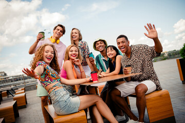 Obraz premium Young friends enjoying outdoor leisure gathering at table with drinks on a sunny day, sharing laughter and fun moments together