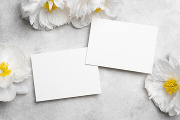 Blank wedding invitation mockup with copy space surrounded by elegant white peonies on a textured...