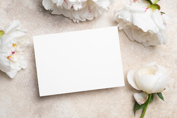 Blank greeting card mockup with copy space surrounded by elegant white peonies on a textured...