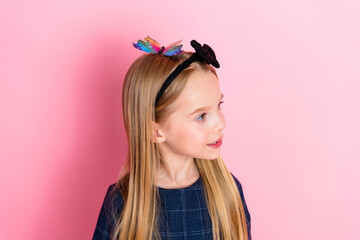 Adorable young girl with colorful hair accessory posing against a pink background in a charming...