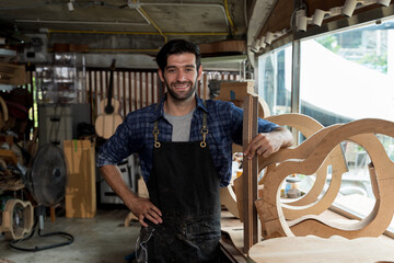Confident luthier smiling in woodworking studio with guitar frames on workbench, wearing flannel shirt and apron