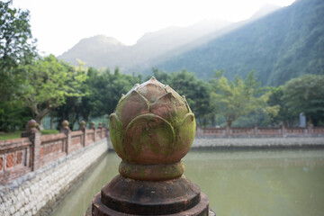 Stone lotus flower decorating a pillar in Bai Dinh temple with mountains and pond in the background