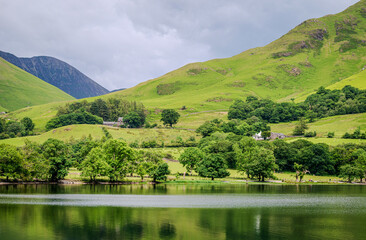 Cropped view of a Buttermere Lake fell with farmhouses on its slopes, layered tree lines, and deep...