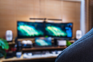 Modern home office setup with ergonomic gray chair, multi-monitor screens, wood desk, and green plants, creating a productive and stylish workspace environment.