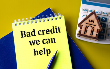 BAD CREDIT WE CAN HELP - words in a yellow notepad with a calculator and a wooden house in the background