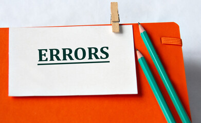 ERRORS - word on a white sheet on an orange notebook and pencils