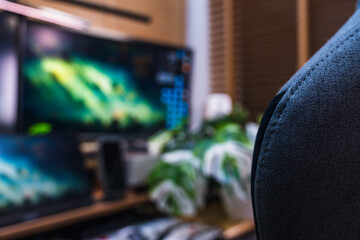 Modern home office setup with ergonomic gray chair, multi-monitor screens, wood desk, and green plants, creating a productive and stylish workspace environment.