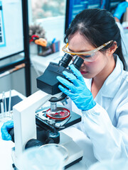 Confident female scientist in lab coat using microscope to analyze sample in petri dish. Concept of...