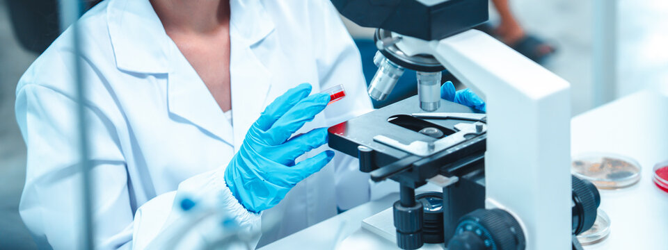 Confident female scientist in lab coat using microscope to analyze sample in petri dish. Concept of women in STEM, scientific research, education, empowerment, and gender diversity in science.