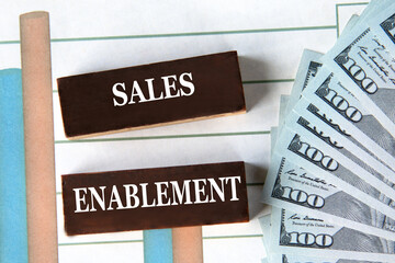 SALES ENABLEMENT - words on brown wooden blocks on the background of a graph and banknotes