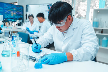Fototapeta premium Young scientist writing experimental results in laboratory. Wearing lab coat, gloves, and safety goggles in modern lab environment with scientific glassware and teamwork in background.