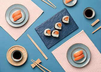 Sushi and sashimi are arranged on plates with chopsticks and soy sauce on a blue table
