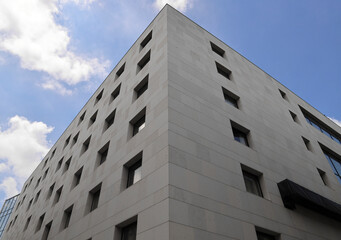 many rows of glass windows frames  on large square grey concrete tiles wall of business office building. angle view. gray tiled exterior. Subotica Serbia City centre Blue cloudy sky heaven