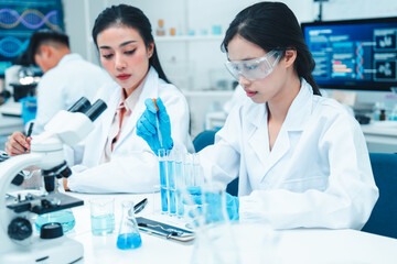 Two female scientists working in a modern laboratory. One is carefully transferring liquid with a...