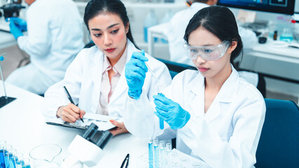 Two female scientists working in a modern laboratory. One is carefully transferring liquid with a...