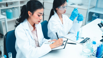 Two female scientists working in a modern laboratory. One is carefully transferring liquid with a...