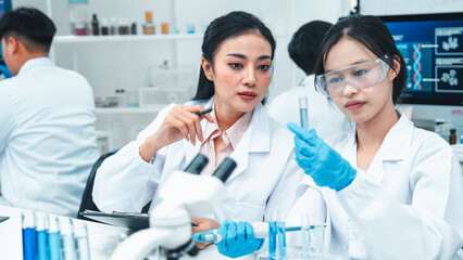 Two female scientists analyzing test tube samples in a laboratory setting. One supervises while the other conducts an experiment. Concept of science education, teamwork, and research collaboration.