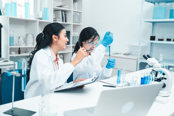 Two female scientists analyzing test tube samples in a laboratory setting. One supervises while the...
