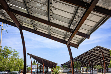 Solar panel arrays installed on metal structures above a parking lot, providing shade while...