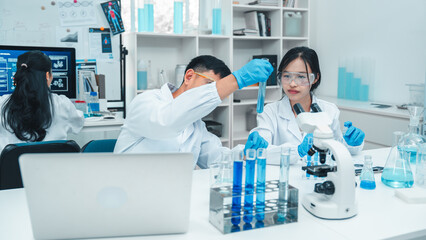 Two scientists in a laboratory working with test tubes. holds up a blue liquid sample while the...