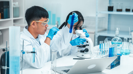 Two scientists in a laboratory working with test tubes. holds up a blue liquid sample while the...