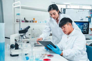 Female senior scientist supervising young male researcher in a modern lab. She reviews data on a...