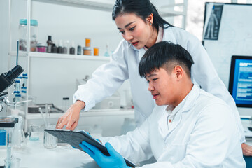 Female senior scientist supervising young male researcher in a modern lab. She reviews data on a...