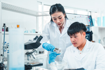Female senior scientist supervising young male researcher in a modern lab. She reviews data on a...