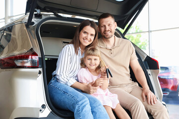 Happy family with keys sitting in car trunk in salon