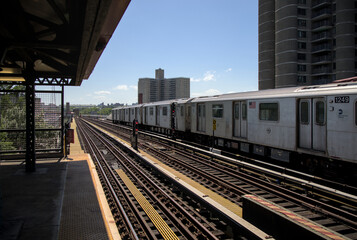 Fototapeta premium train passing in front of high rise apartment tower buildings in the bronx new york city (low income real estate highrises) elevated subway platform stop four parkway