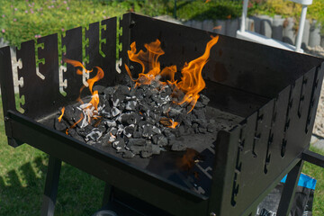 Bright flames igniting charcoal in a black barbecue grill, concept of outdoor cooking, summer, party