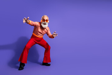 Elderly man's retro-inspired dance pose in vibrant vintage clothing against a bold purple backdrop