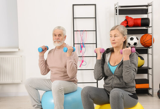 Elderly couple exercising with dumbbells and fitness balls at home