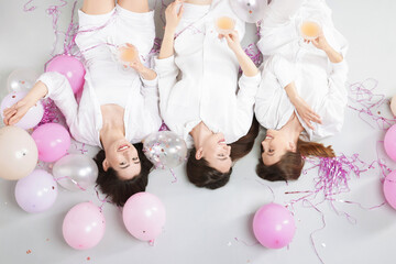 Pajama party. Happy friends with glasses of alcoholic drink, balloons and tinsel on grey...