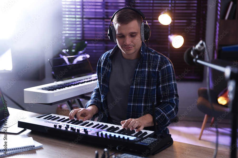 Poster man in headphones working with midi keyboard at table in home studio