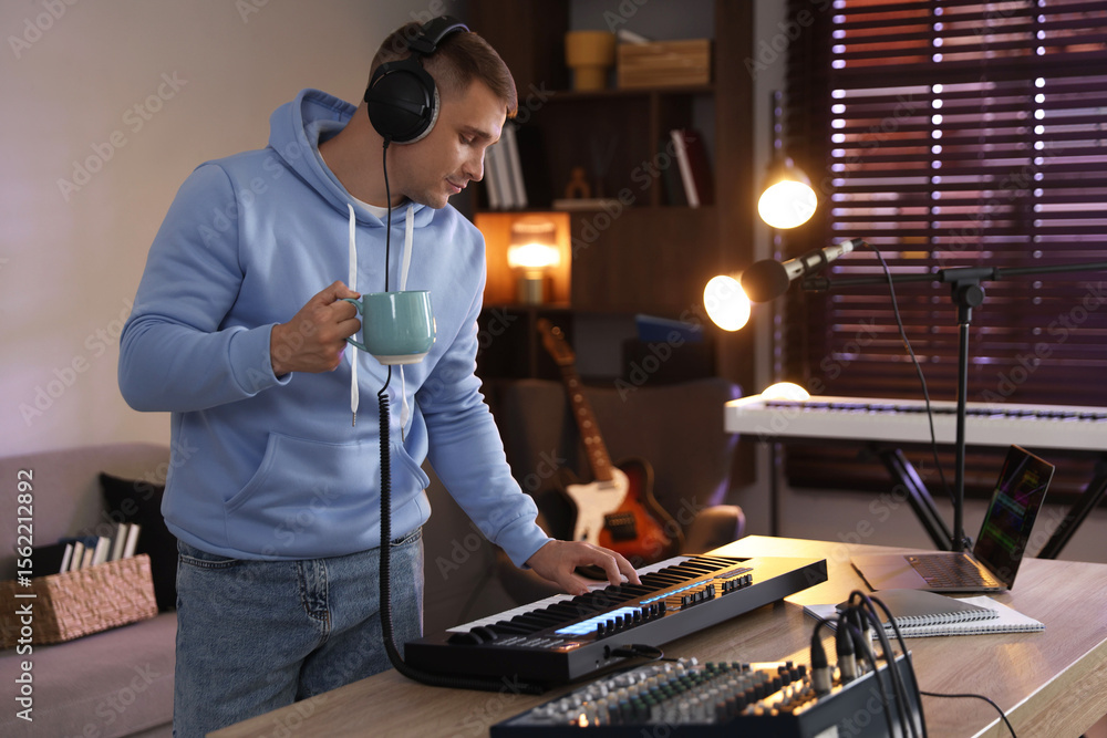 Poster man in headphones working with midi keyboard at table in home studio