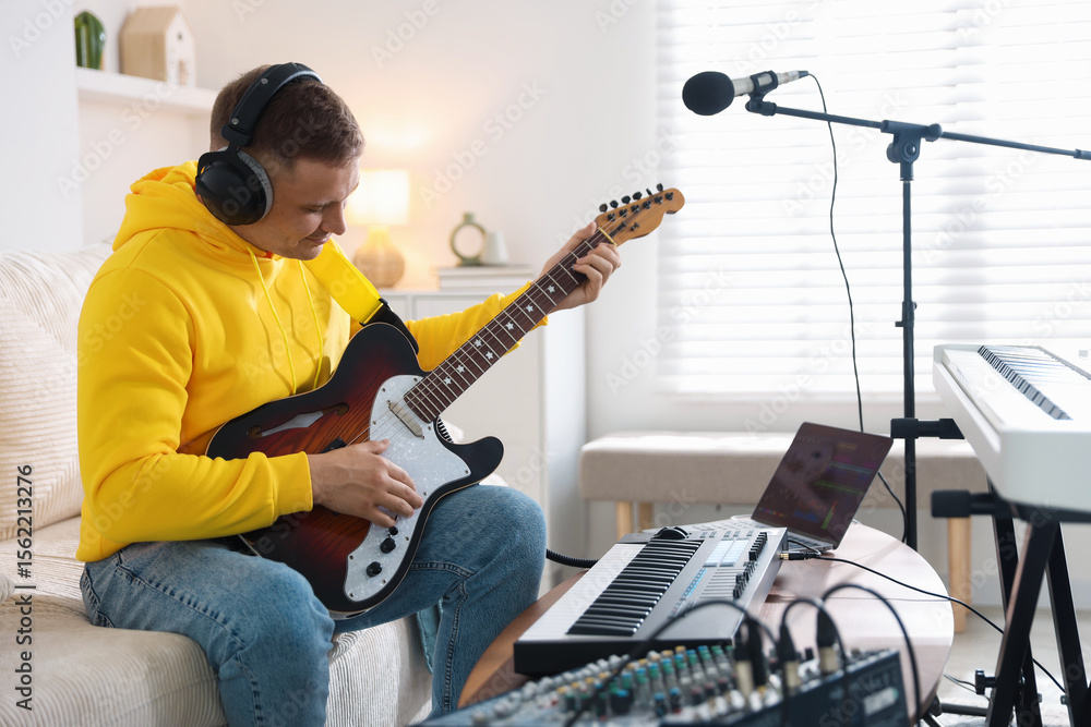 Poster man in headphones working with guitar and midi keyboard at table in home studio