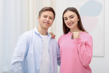 Happy couple with key of their new apartment indoors