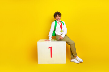 Charming student with backpack and medal on podium against yellow background representing academic...