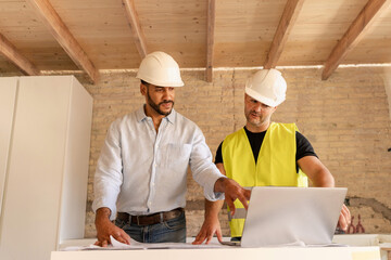 Construction workers discussing renovation house with investor using laptop at building site